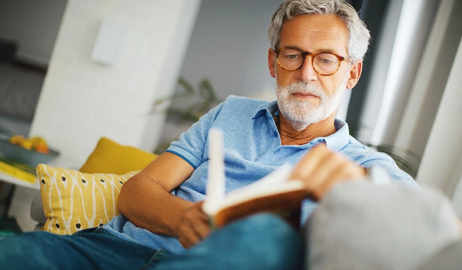 Älterer Mann sitzt auf dem Soaf und liest ein Buch.